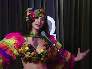 The hosts of Playboy Radio's Morning Show are looking at their guest model who is wearing the costume she'll be wearing to the Playboy Mansion for Halloween. Her head and tits are covered in fake fruit like oranges, limes, lemons, and more. She flashes her breasts for the hosts and viewers.